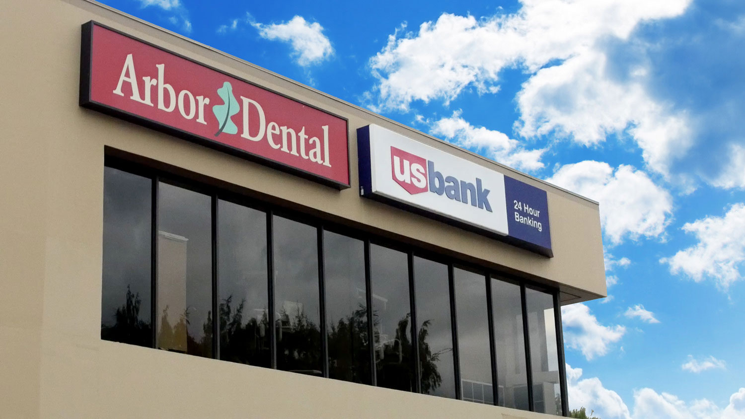 The image shows a sign with the text Arbor Dental on the front of a building, which appears to be a dental clinic, under a blue sky with clouds.