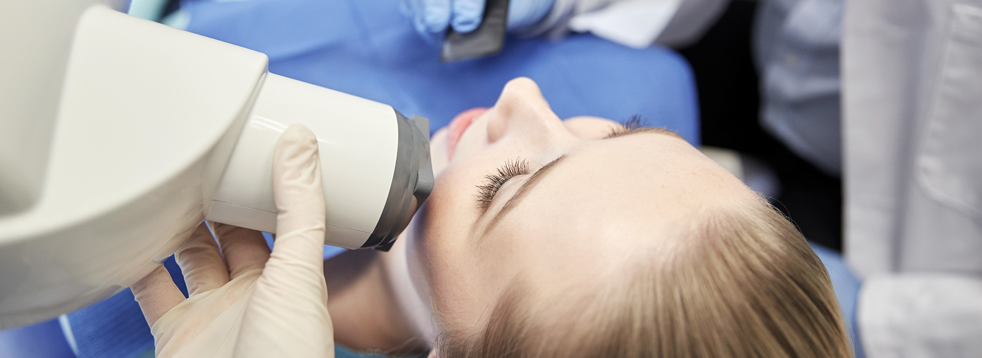 A person receiving dental treatment under a magnifying lamp with medical professionals observing through a microscope.