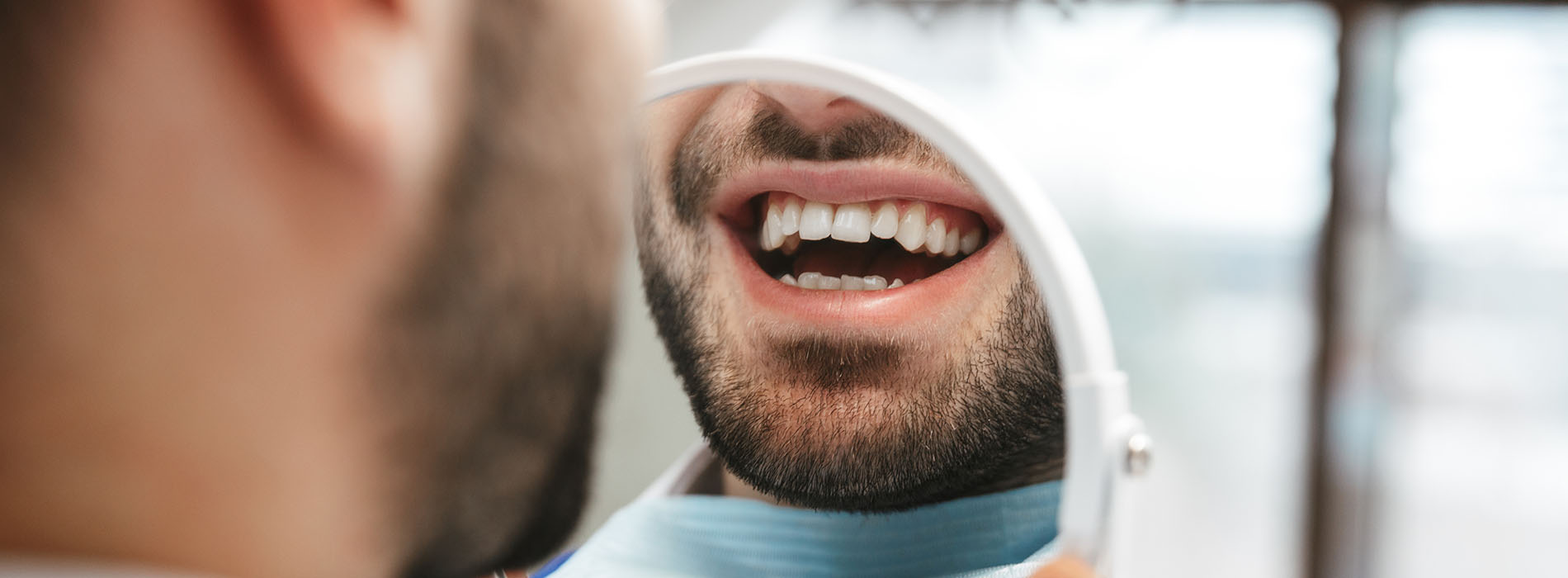 This image features a man with a beard sitting in front of another person who appears to be a dental professional, possibly during a dental appointment, with a clear focus on oral hygiene.