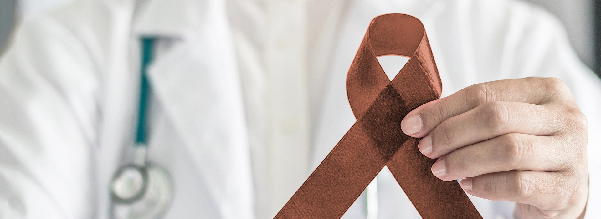 The image shows a person holding a red ribbon with a white cross on it against a medical background, suggesting awareness for a health issue.